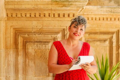 Donatella Briganti sorridente con foglio e penna, in procinto di scrivere