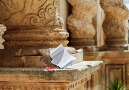 Un block notes e una penna sulla base della colonna tortile di una chiesa barocca di Palazzolo Acreide